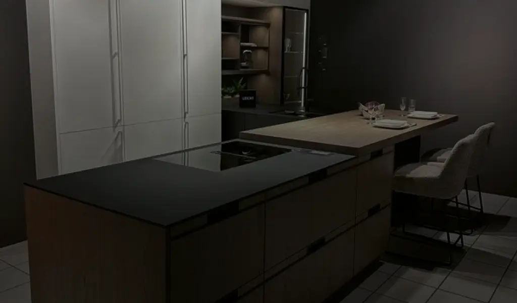 Elegante Leicht Küche mit Kochinsel, Holz- und Steinoptik sowie moderner Essplatzlösung. Rechts im Bild der exklusive Leicht Showroom bei Nacht. Hochwertige Designküche mit Stil und Funktionalität.